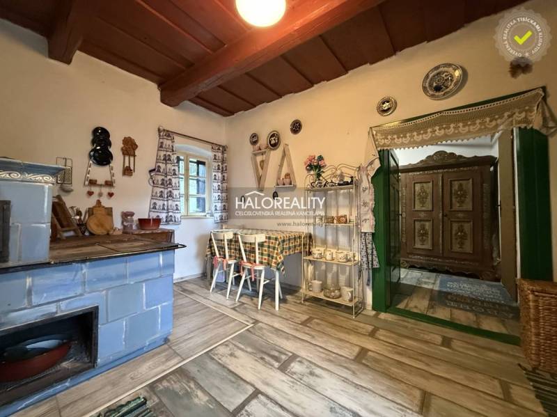 A rustic kitchen in a cottage with a blue stove, decorative plates, and a wooden-patterned floor.