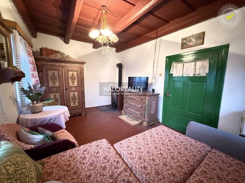 Rustic interior of a cottage with wooden beams, antique furniture, and green doors.