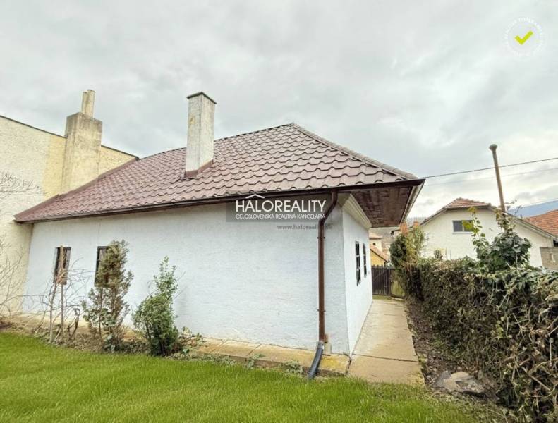 A cottage in Horná Ves with a white facade, a sloped roof, and a well-maintained garden.