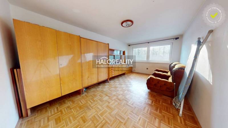 A room with furniture and a wooden decor floor in a family house, illuminated by large windows.