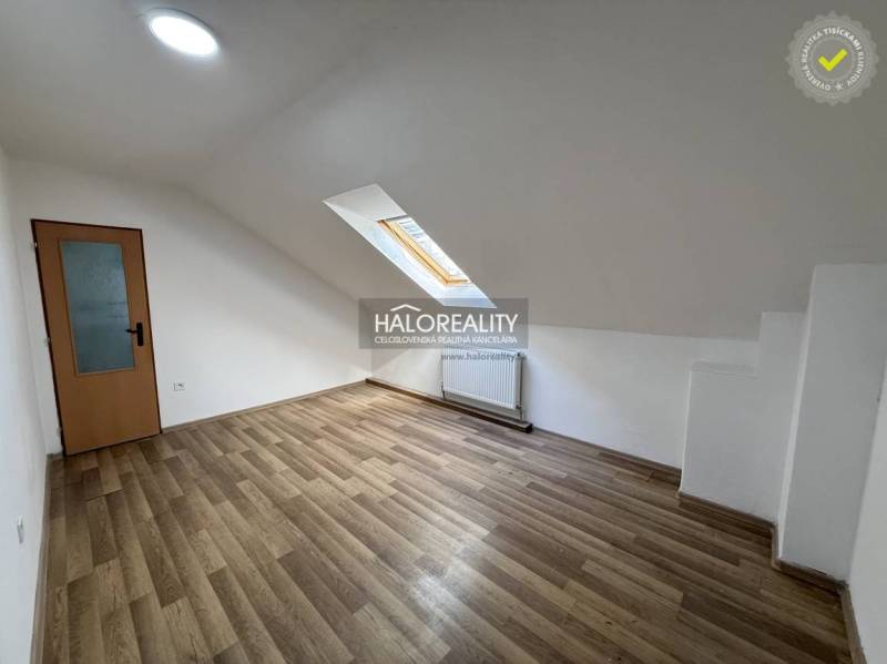A studio apartment with a wooden floor, a skylight, and white walls.