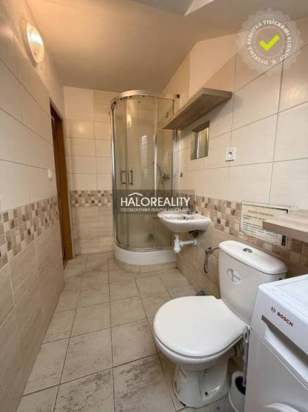 A studio apartment bathroom with a toilet, shower, and tiles in neutral tones.