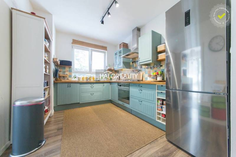 A kitchen in a 3-room apartment with a wooden decor floor, a large refrigerator, and light.