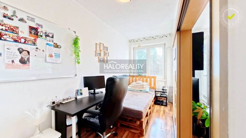 A room in a 3-room apartment with a wooden decor floor, a desk, and a bed.