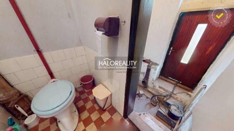 Bathroom in a family house with a toilet, a bucket, and a tiled floor.