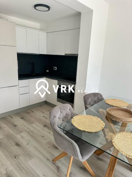 Recreational apartment with a kitchen, glass table, and wooden decor flooring.