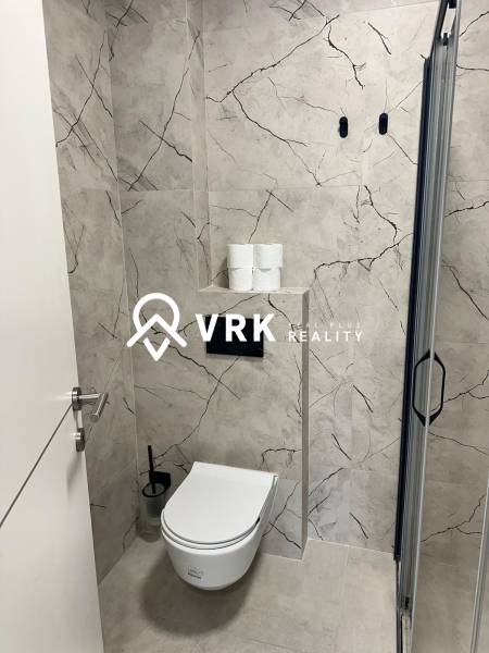 A bathroom in a holiday apartment with a toilet and a shower, surrounded by marble tiles.