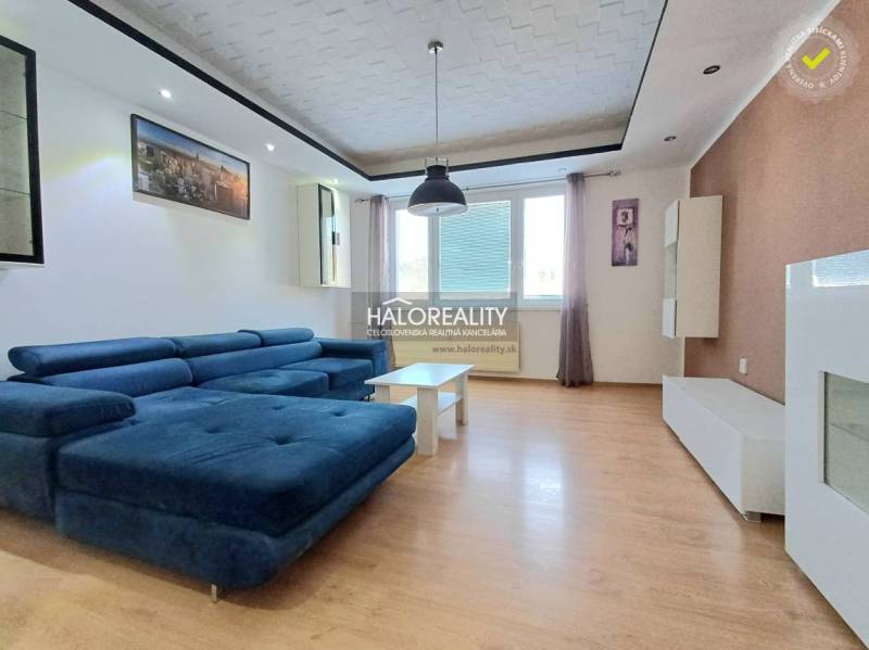 Living room in a three-room apartment with a wooden decor floor and a blue sofa.