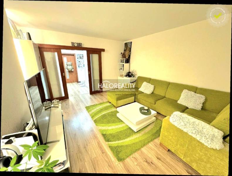 Living room with a sofa and wood-patterned flooring in a three-room apartment.