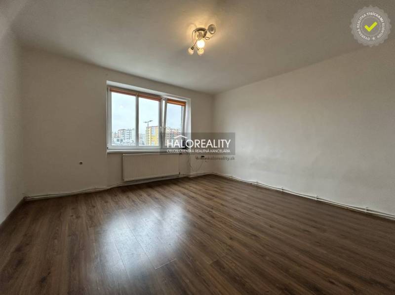 A room in a 2-bedroom apartment with a wooden decor floor and a large window.