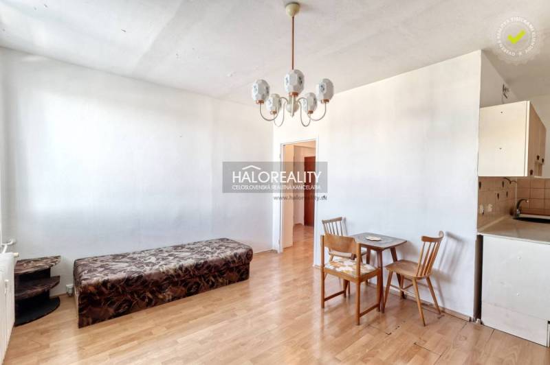 Living area in a two-room apartment with wood-patterned flooring, a sofa set, and a dining table.