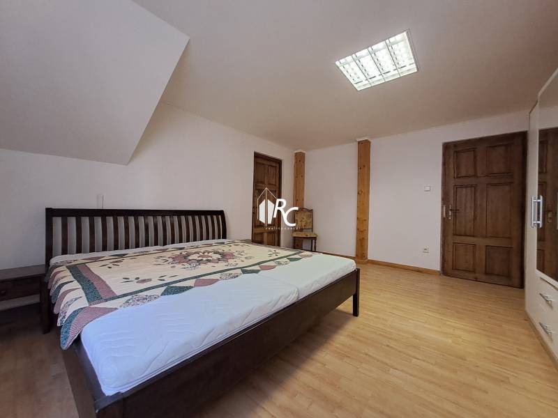 A bedroom with wood-patterned flooring, a bed, and a large mirror in a three-room apartment.