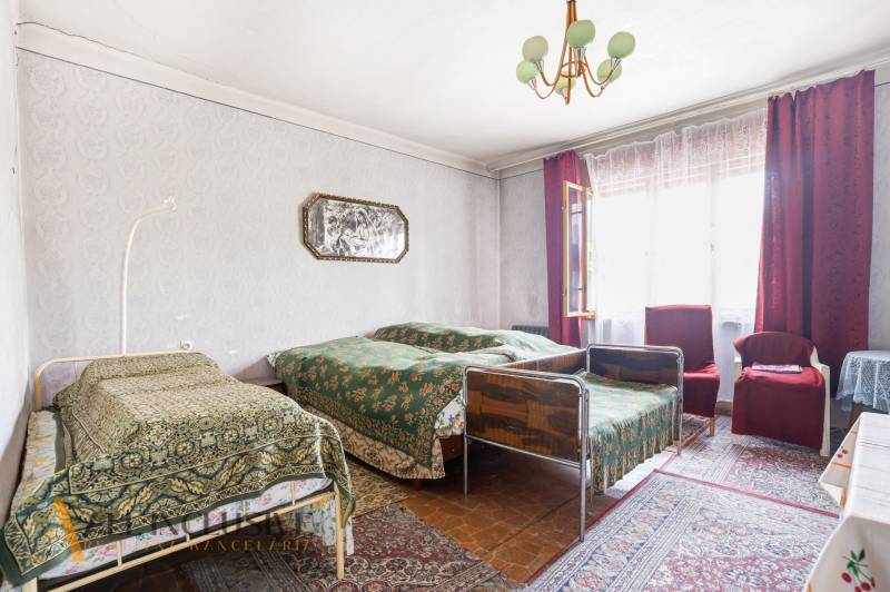 A room in a family house with three beds, carpets, and a large window with curtains.