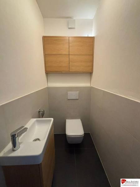 Bathroom with toilet, sink, and cabinet in a 3-room apartment, floor with wood decor.