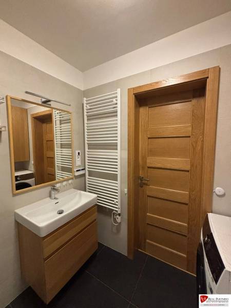 Bathroom with a sink, mirror, radiator, and cabinets in a 3-room apartment.
