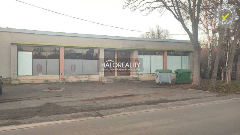 A single-story building with glass panels, in front of it are stands with containers. Commercial premises.