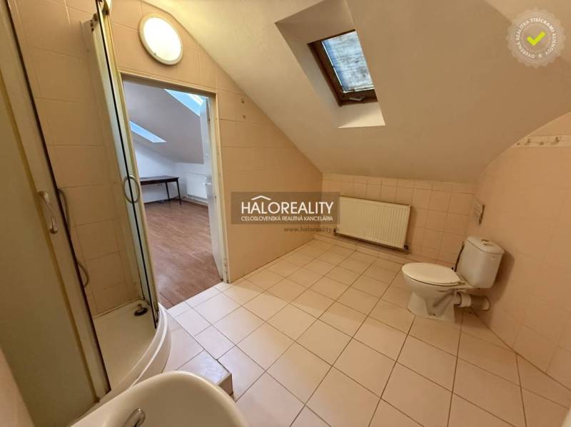 A bathroom in a studio apartment with a corner shower and tiles, floor with a wooden decor.