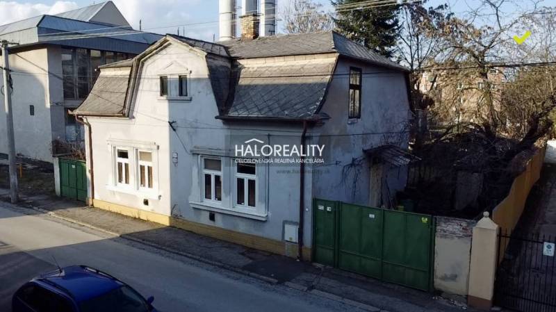 A family house in Rimavská Sobota with a classic roof design, a large gate, and neighboring buildings.