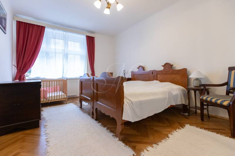 A bedroom in a three-room apartment with a wooden decor floor, a crib, and red curtains.