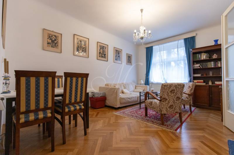 Living room with a sofa, bookshelf, chairs, wooden decor flooring, and a chandelier in a three-room apartment.