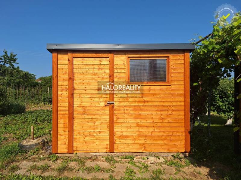 A wooden garden house in the Gardens in Bojnice surrounded by greenery under a blue sky.