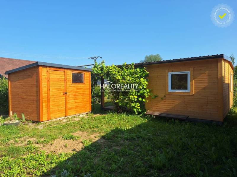 Wooden garden houses in the Gardens of Bojnice, surrounded by greenery and blue sky.