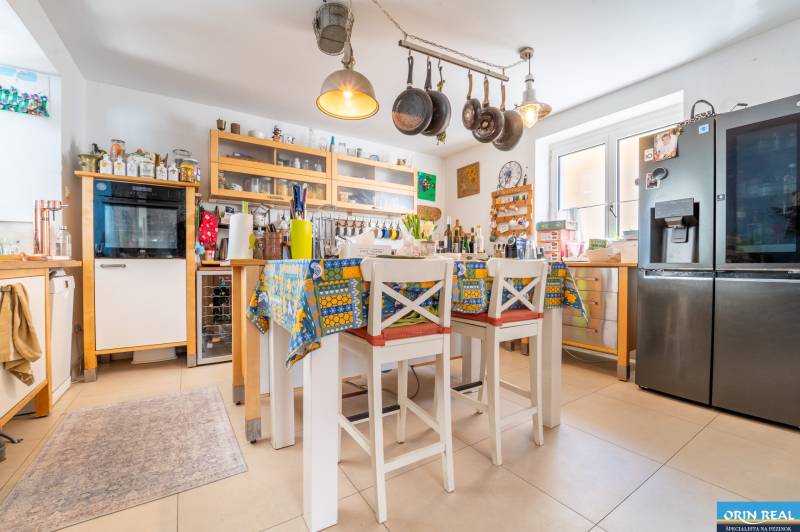 A kitchen in a family house with hanging pans, a colorful tablecloth, and modern appliances.