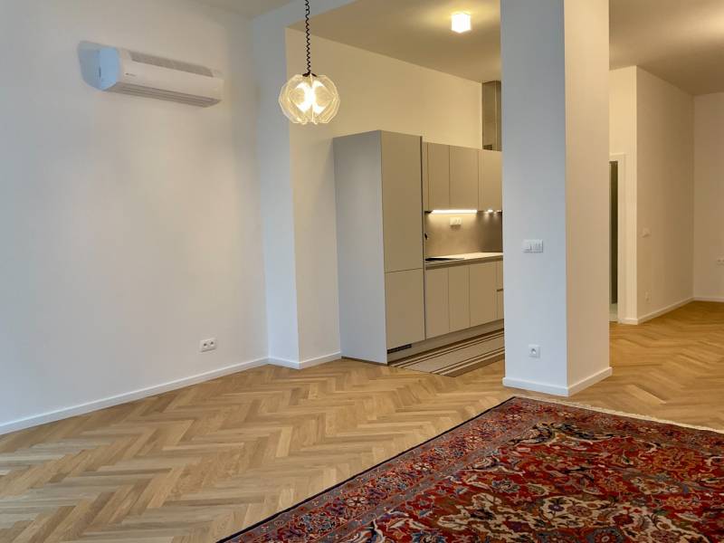 Living room with kitchen, bright interior, wooden decor flooring, hanging light fixture.