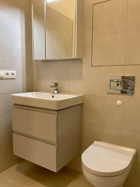 Bathroom in a 2-room apartment with a sink, cabinet, and mirror, neutral tiles.