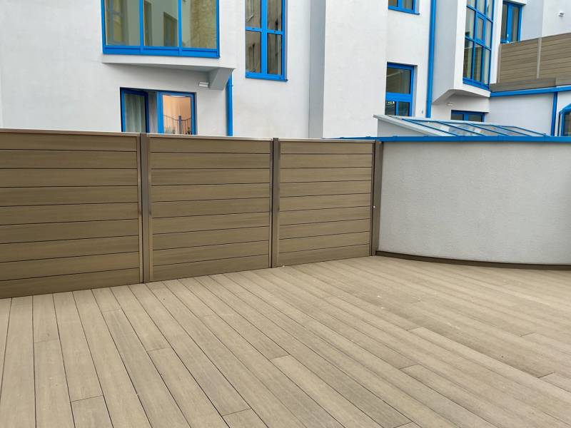 Enclosed terrace with wood-patterned flooring and blue window frames of the building.