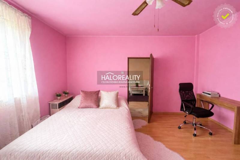 A bedroom with pink walls, a desk, and a wood-patterned floor in a family house.