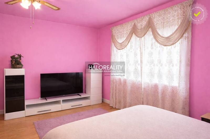 Pink bedroom in a family house with a TV, wood-patterned flooring, and curtains.