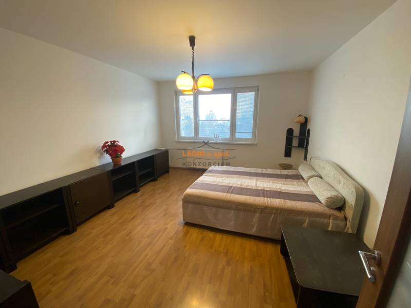 A room in a three-room apartment with a bed, dark furniture, and a floor with a wood decor.