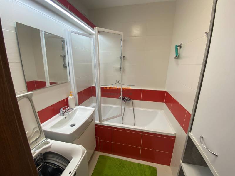 A bathroom in a 3-room apartment with a bathtub, washing machine, and red and white tiles.