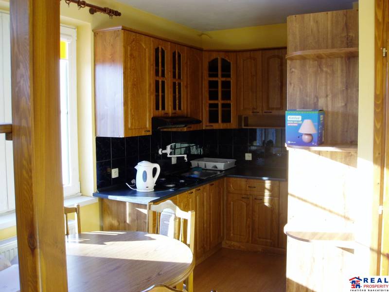A kitchen with wooden cabinets and black tiles in a two-room apartment.