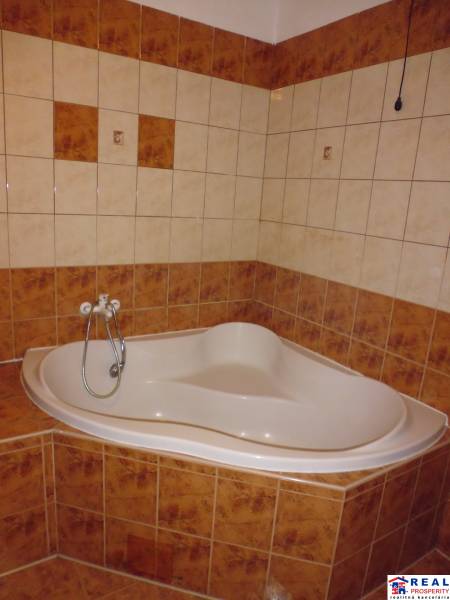 A rounded bathtub and tiles in the bathroom of a 2-room apartment with brown elements.