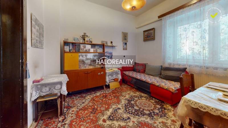A room in a family house with retro furniture, a floral carpet, and lace curtains.