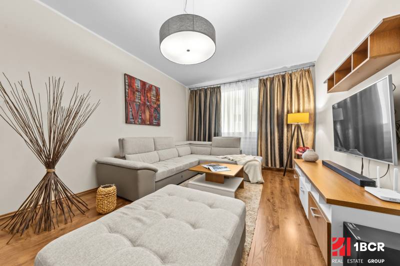 Living room in a three-room apartment with a wooden decor floor and a gray sofa.