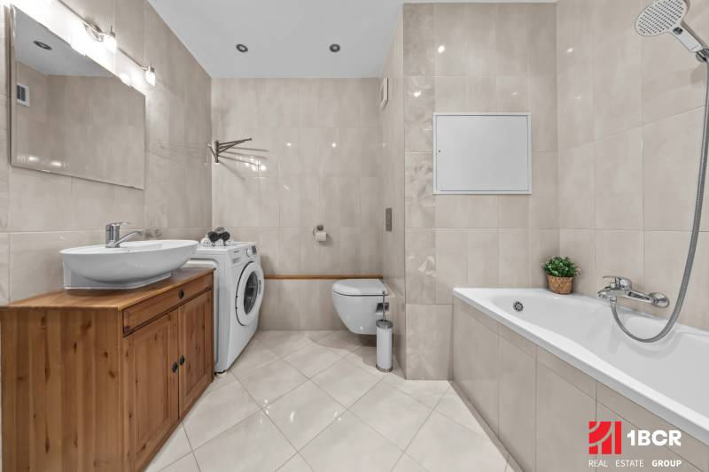 A bathroom in a 3-room apartment with a bathtub, washing machine, cabinet, and ceramic tiles.