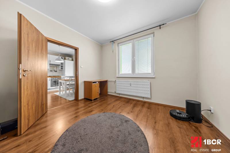 A room in a 3-room apartment with a wooden decor floor and an entrance to the kitchen.