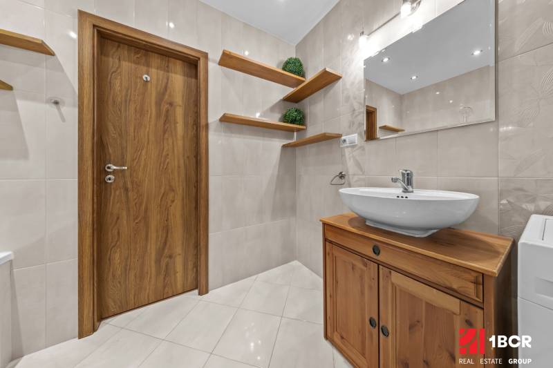 A bathroom in a three-room apartment with light tiles and wooden elements.