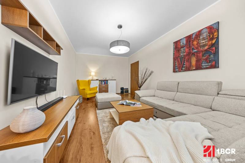 Living room in a 3-room apartment with a wooden decor floor, gray sofa, and yellow armchair.