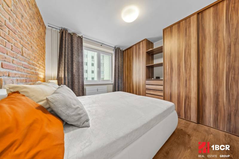 A bedroom in a 3-room apartment with a wooden decor floor and a brick wall.
