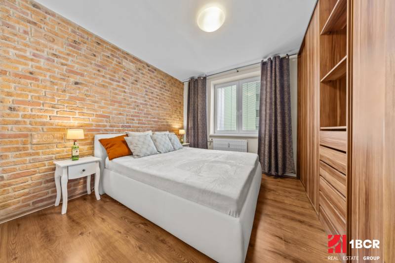 Bedroom in a 3-room apartment with a brick wall and a wooden decor floor.