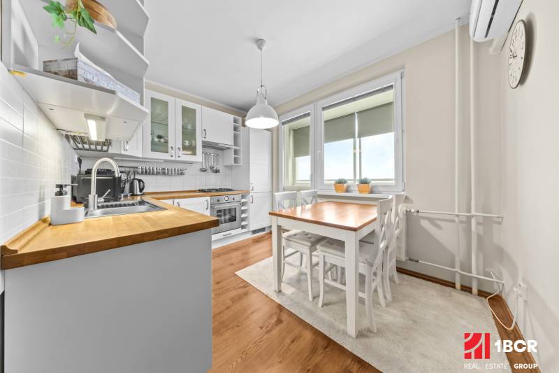 A kitchen in a 3-room apartment with white furnishings and a wooden decor floor.
