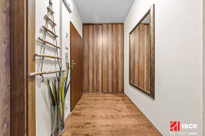 A hallway in a 3-room apartment with a wooden decor floor, a large mirror, and decoration.