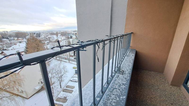 A balcony with Christmas lights, a snow cover, and a view of Poprad and family houses.