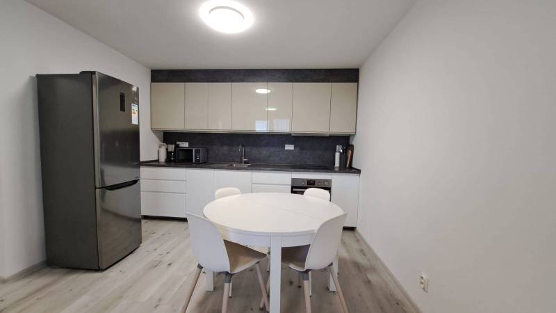 A kitchen in a family house with a refrigerator, a round table, and a floor with a wooden decor.