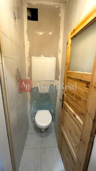 A toilet with wooden doors in a 3-room apartment, incomplete tiles, and a white floor.