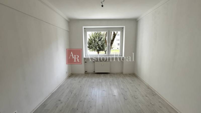 A room with a large window, a floor with a wooden decor, a 3-room apartment.